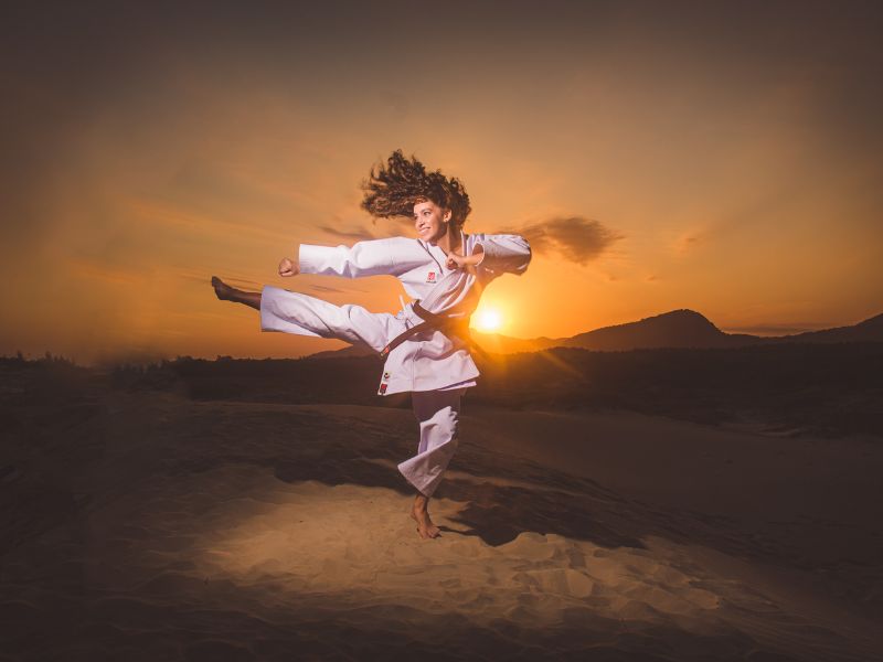 Karate-Kämpferin führt einen beeindruckenden Sprungkick bei Sonnenuntergang aus, symbolisierend für die Kraft, Eleganz und Freiheit im Karate Kumite.