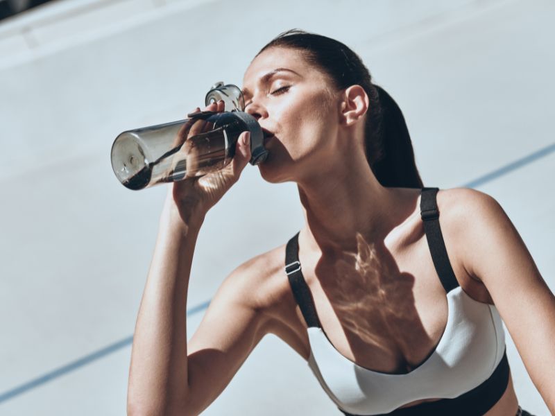 Karateka trinkt Wasser aus einer Flasche nach einem intensiven Training, symbolisierend für die Wichtigkeit von Hydration und Erholung im Karate Kumite.