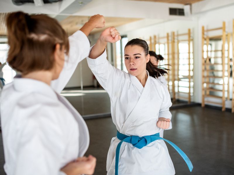 Zwei Karate-Schülerinnen im Dojo üben konzentriert Schlag- und Blocktechniken, symbolisierend für Training, Disziplin und die Kunst des Karate Kumite.