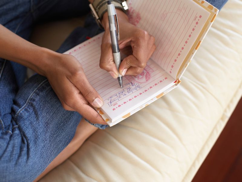 Eine Person schreibt in ein Tagebuch, eine meditative und reflektierende Hobby Idee zur Stressbewältigung und persönlichen Entwicklung.