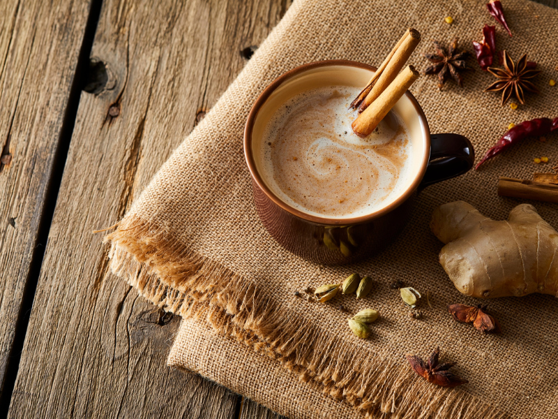 Tasse Chai Latte mit Zimtstangen, Ingwer und Kardamom auf Holztisch – wärmende Hygge Idee im Herbst