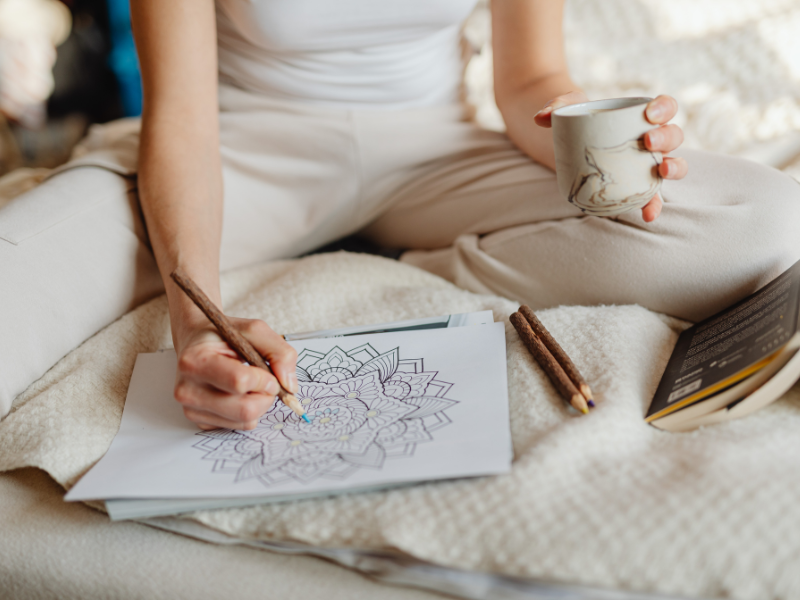 Frau sitzt gemütlich mit Tee und malt Mandala – kreative Hygge Idee Herbst für Entspannung
